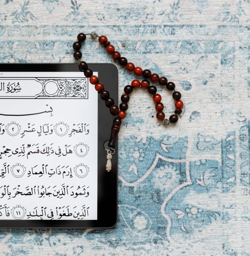 A tablet displaying the Quran on a prayer rug with prayer beads beside it.